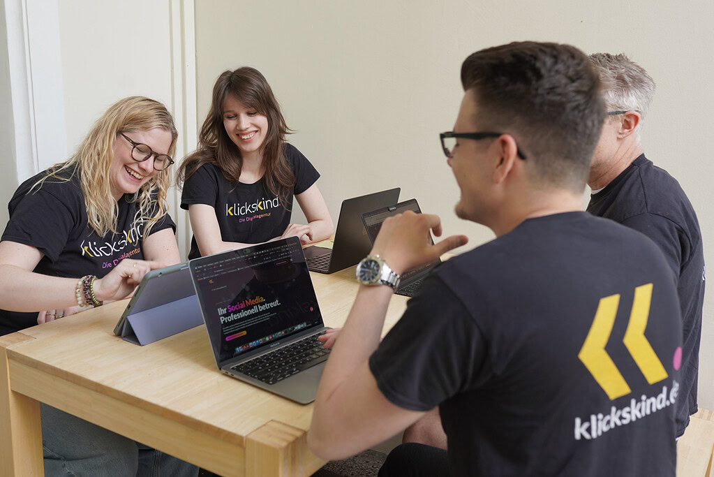 Vier Mitglieder des klickskind-Teams sitzen gemeinsam am Tisch und arbeiten mit Laptops und Tablets.