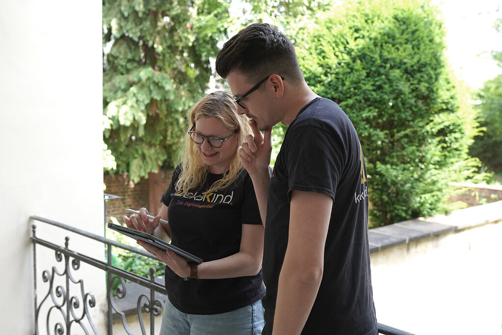 Zwei Mitglieder des klickskind-Teams arbeiten gemeinsam an einem Tablet im Freien.