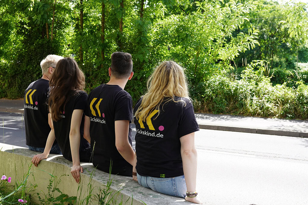 Vier Mitglieder des klickskind-Teams sitzen draußen nebeneinander und tragen schwarze klickskind-Shirts.