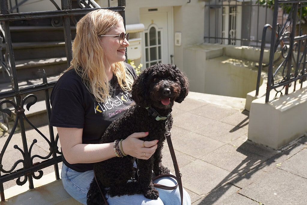 klickskind-Mitarbeiterin sitzt draußen mit einem schwarzen Hund auf dem Schoß.