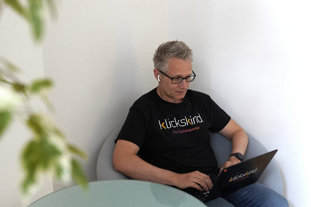 Mitarbeiter von klickskind sitzt mit Laptop in einem Sessel und arbeitet.